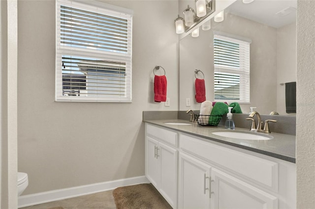 full bath featuring double vanity, baseboards, toilet, and a sink