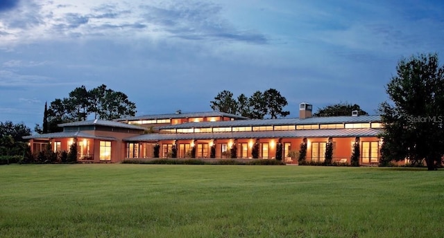 back of property featuring a standing seam roof, a yard, a chimney, and metal roof