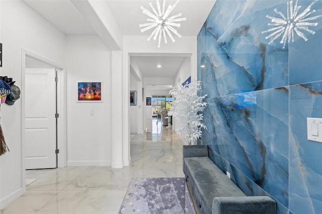 hallway with baseboards, marble finish floor, and a notable chandelier