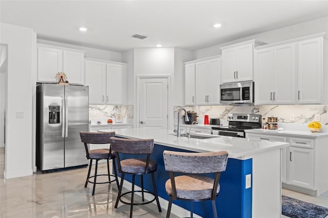 kitchen featuring a breakfast bar area, stainless steel appliances, a sink, visible vents, and a center island with sink