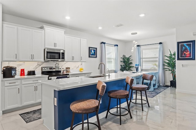 kitchen featuring stainless steel appliances, white cabinets, a sink, an island with sink, and a kitchen bar