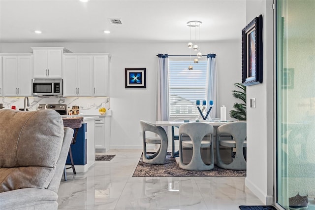 kitchen featuring stainless steel microwave, open floor plan, marble finish floor, white cabinetry, and backsplash