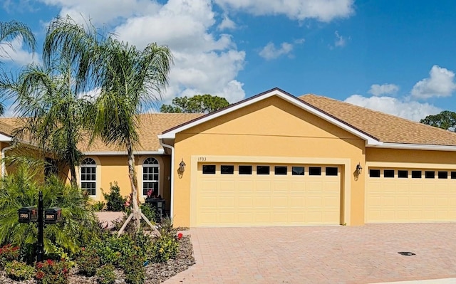 ranch-style home with roof with shingles, decorative driveway, an attached garage, and stucco siding