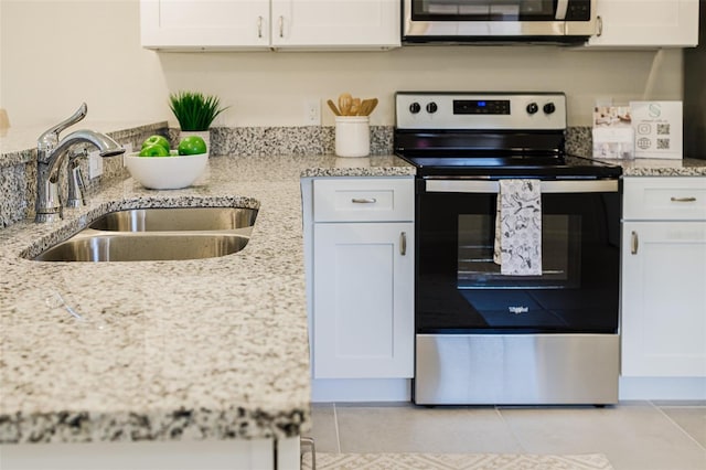 kitchen featuring appliances with stainless steel finishes, white cabinets, a sink, and light stone counters