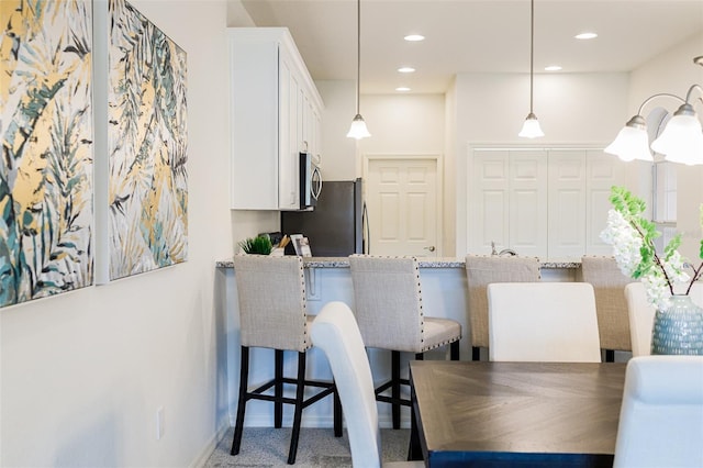 kitchen featuring stainless steel appliances, a kitchen breakfast bar, white cabinets, and decorative light fixtures