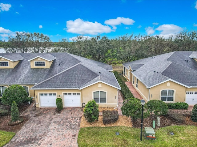 view of front facade featuring roof with shingles, decorative driveway, and stucco siding