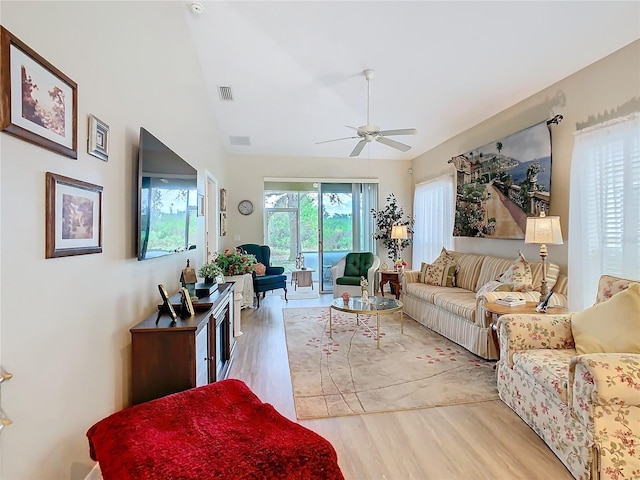 living room featuring light wood finished floors, visible vents, vaulted ceiling, and a ceiling fan