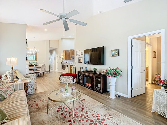 living area with ceiling fan with notable chandelier, visible vents, a towering ceiling, baseboards, and light wood finished floors