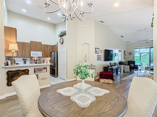 dining area with light wood-style flooring, high vaulted ceiling, baseboards, and ceiling fan with notable chandelier