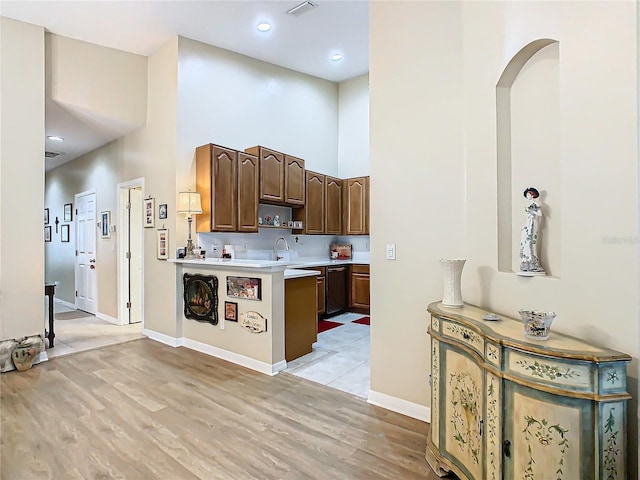 kitchen with light countertops, light wood-type flooring, a towering ceiling, and baseboards