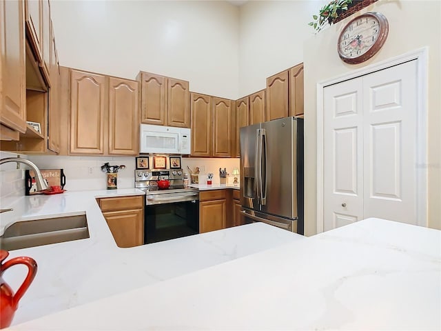 kitchen featuring appliances with stainless steel finishes, a sink, backsplash, and a high ceiling