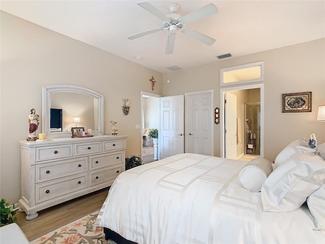 bedroom featuring light wood-type flooring, ensuite bath, visible vents, and ceiling fan