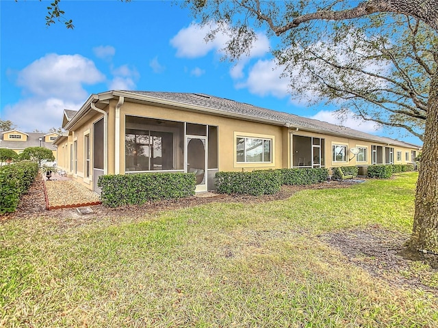 back of property with a yard, a sunroom, and stucco siding