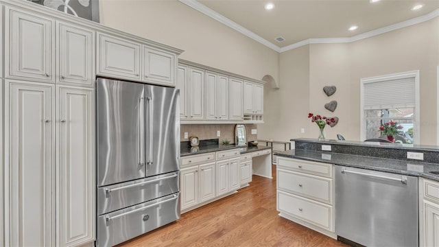 kitchen with appliances with stainless steel finishes, light wood-type flooring, dark stone counters, and crown molding