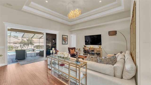 living area with hardwood / wood-style flooring, crown molding, a raised ceiling, and a sunroom