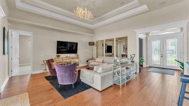 living area with a tray ceiling, french doors, visible vents, and wood finished floors