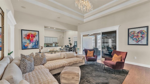 living room featuring a tray ceiling, a notable chandelier, crown molding, wood finished floors, and baseboards