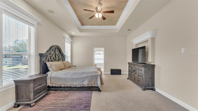 carpeted bedroom featuring a raised ceiling, multiple windows, crown molding, and baseboards