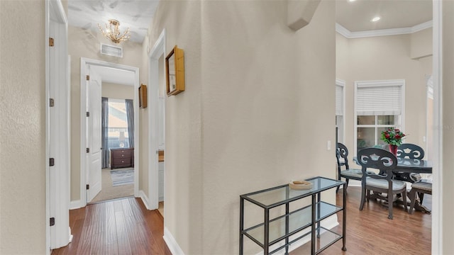 hall with crown molding, a notable chandelier, visible vents, wood finished floors, and baseboards