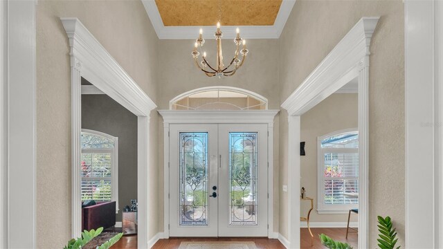 foyer entrance featuring french doors, a notable chandelier, a towering ceiling, wood finished floors, and baseboards