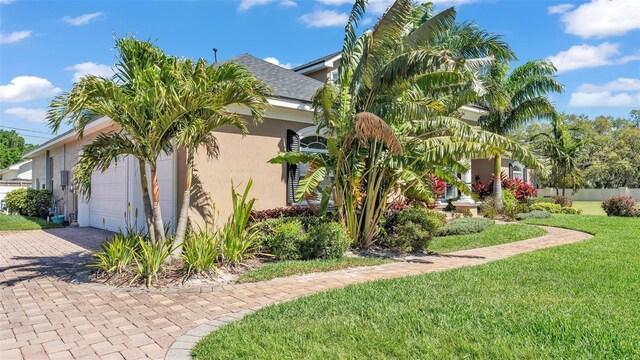 view of side of home with a garage, fence, decorative driveway, a yard, and stucco siding