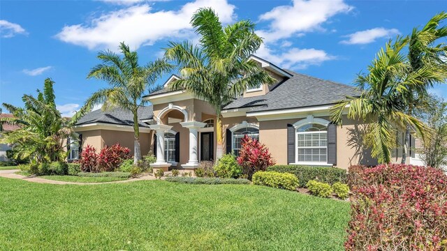 mediterranean / spanish-style home with roof with shingles, a front yard, and stucco siding