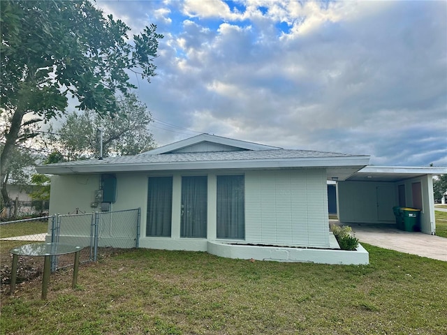 rear view of property featuring an attached carport, fence, concrete driveway, a lawn, and stucco siding