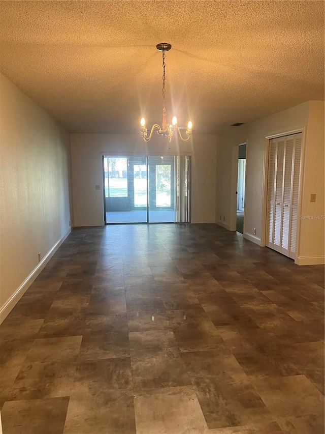 empty room with a chandelier, a textured ceiling, and baseboards