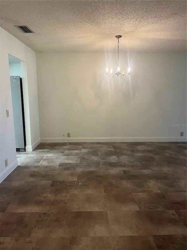 spare room featuring baseboards, a textured ceiling, visible vents, and an inviting chandelier