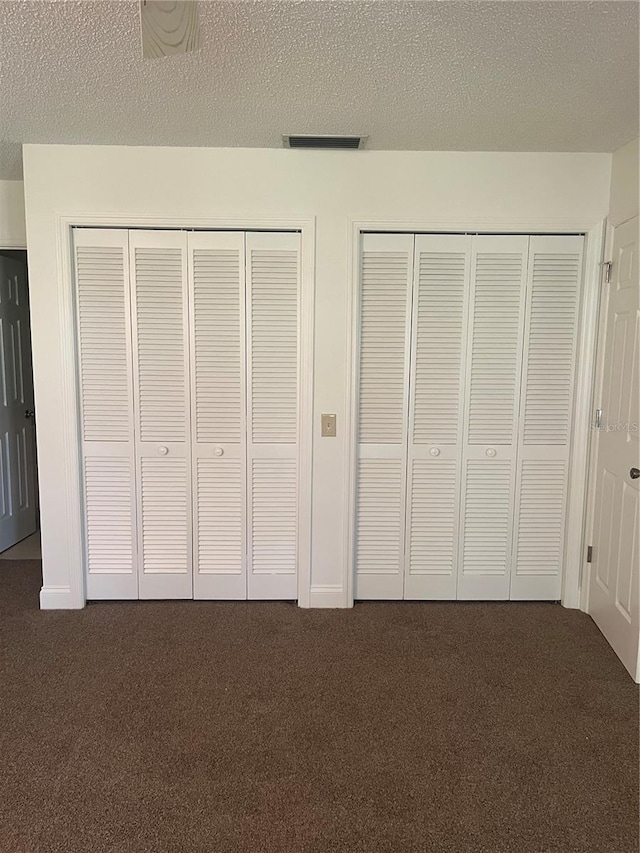 unfurnished bedroom with multiple closets, dark colored carpet, visible vents, and a textured ceiling