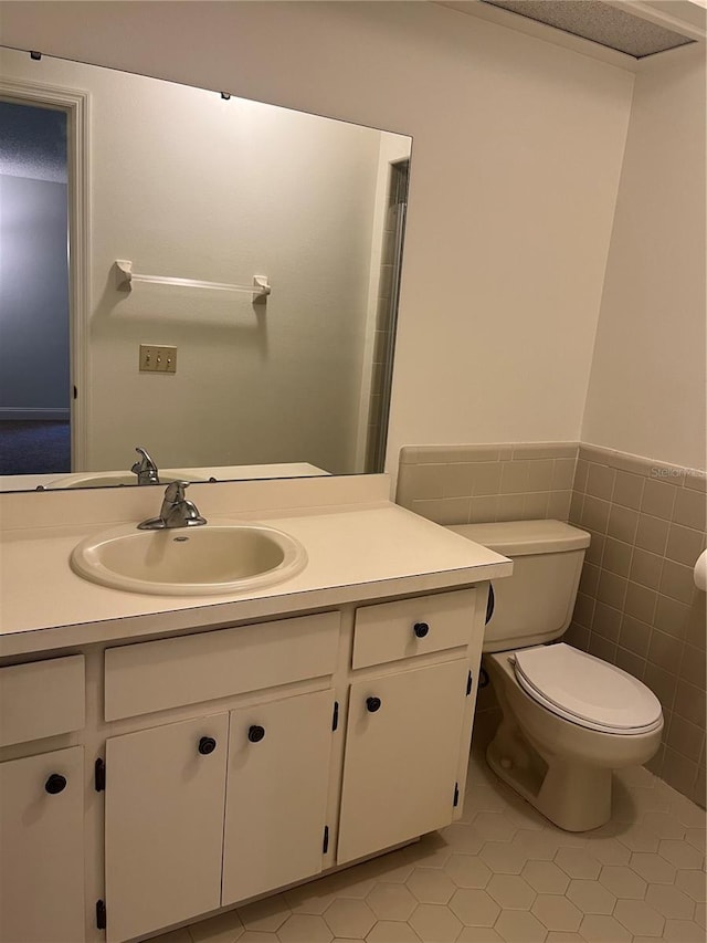 half bath with toilet, a wainscoted wall, tile patterned flooring, vanity, and tile walls