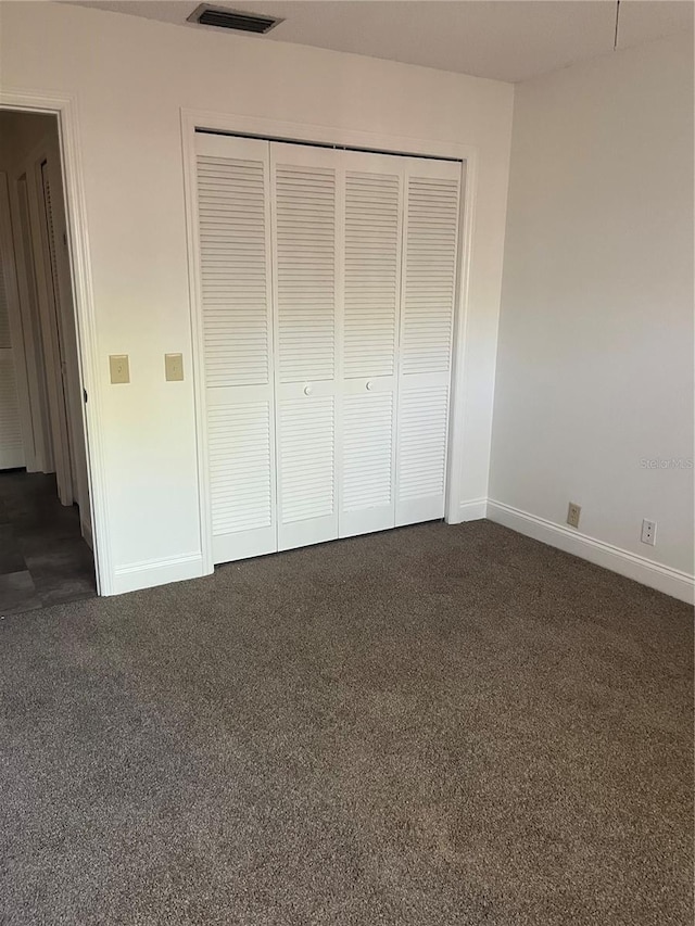 unfurnished bedroom featuring a closet, dark carpet, visible vents, and baseboards