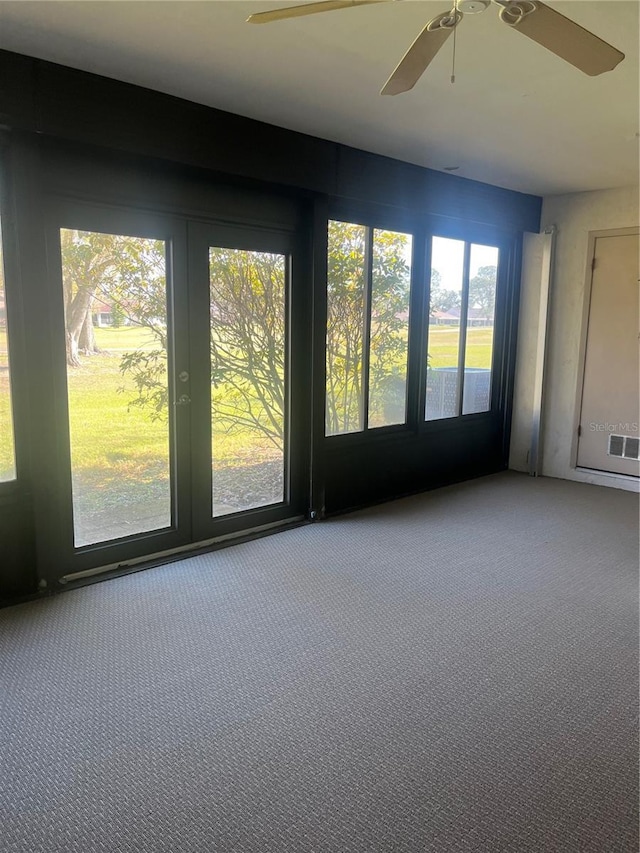 spare room featuring a sunroom, carpet, visible vents, and a ceiling fan