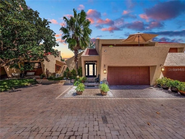 adobe home featuring a garage, decorative driveway, and stucco siding