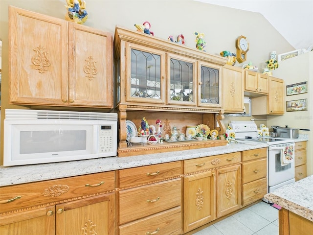 kitchen featuring light tile patterned floors, white appliances, vaulted ceiling, light brown cabinetry, and glass insert cabinets