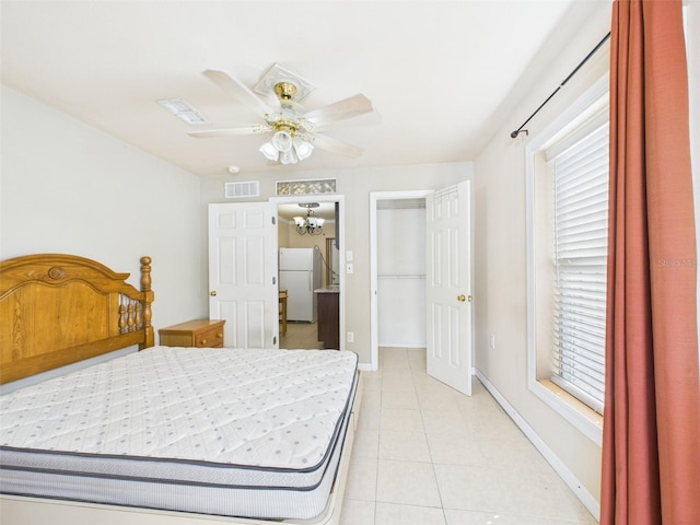 bedroom featuring light tile patterned floors, visible vents, baseboards, freestanding refrigerator, and a walk in closet