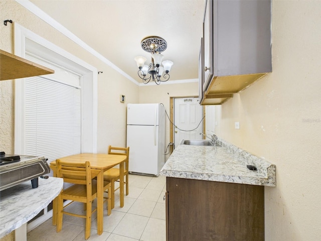 kitchen with a notable chandelier, light countertops, ornamental molding, freestanding refrigerator, and light tile patterned flooring