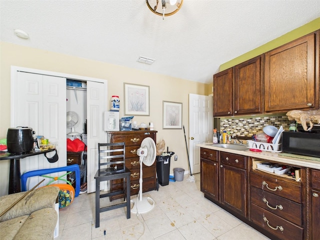 kitchen with black microwave, a sink, visible vents, light countertops, and backsplash