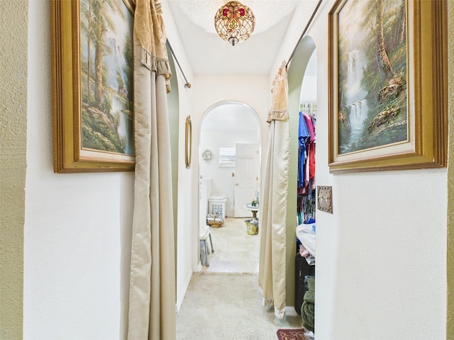 hallway with arched walkways and light colored carpet