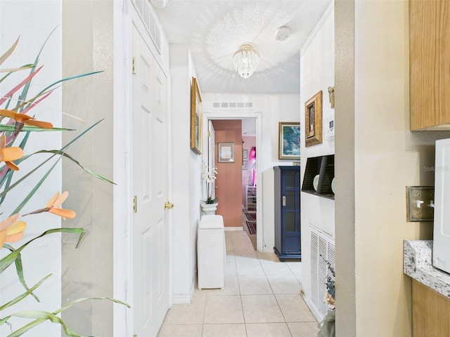 hallway with visible vents, a textured ceiling, and light tile patterned flooring