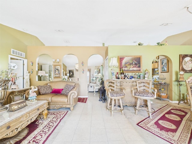 living area with arched walkways, visible vents, vaulted ceiling, a bar, and tile patterned floors