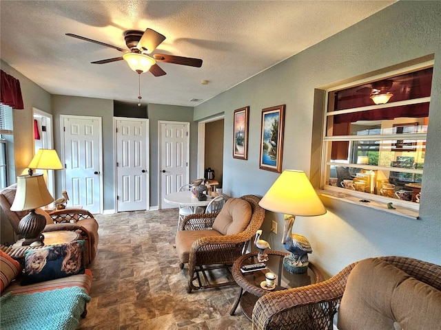 living area with a textured ceiling, ceiling fan, stone finish floor, and baseboards