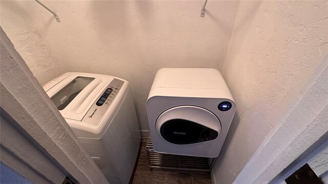 clothes washing area with laundry area, separate washer and dryer, and a textured wall