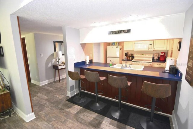 bar featuring dark wood-style floors, a sink, a textured ceiling, white appliances, and baseboards