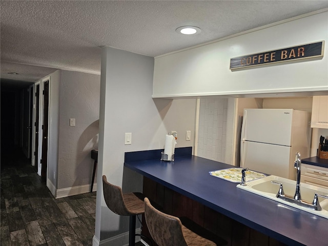 office area featuring a textured wall, dark wood-type flooring, a sink, a textured ceiling, and baseboards