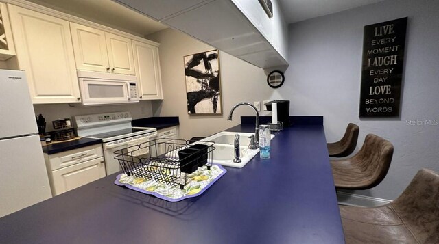 kitchen featuring dark countertops, white cabinetry, a sink, tile patterned flooring, and white appliances