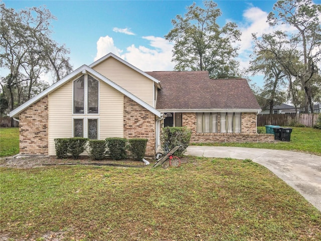 mid-century inspired home with driveway, fence, a front lawn, and brick siding