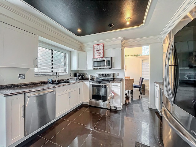 kitchen featuring dark countertops, ornamental molding, stainless steel appliances, white cabinetry, and a sink