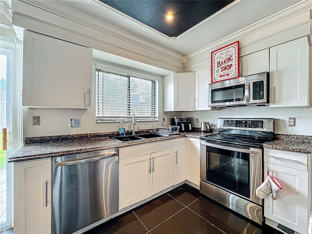 kitchen featuring crown molding, stainless steel appliances, dark countertops, a sink, and dark tile patterned flooring