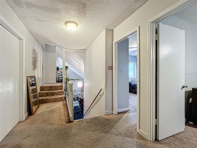 corridor with an upstairs landing, stairs, a textured ceiling, and carpet flooring